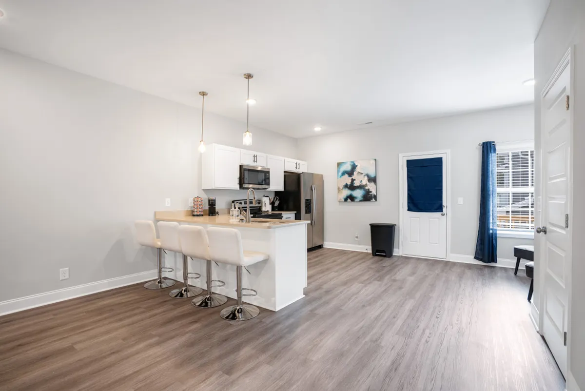 A modern kitchen with a central island and bar stools is bathed in natural light. The space flows into adjacent living areas, and artistic touches add warmth. This perspective highlights where family and friends can share meals or casual conversations.