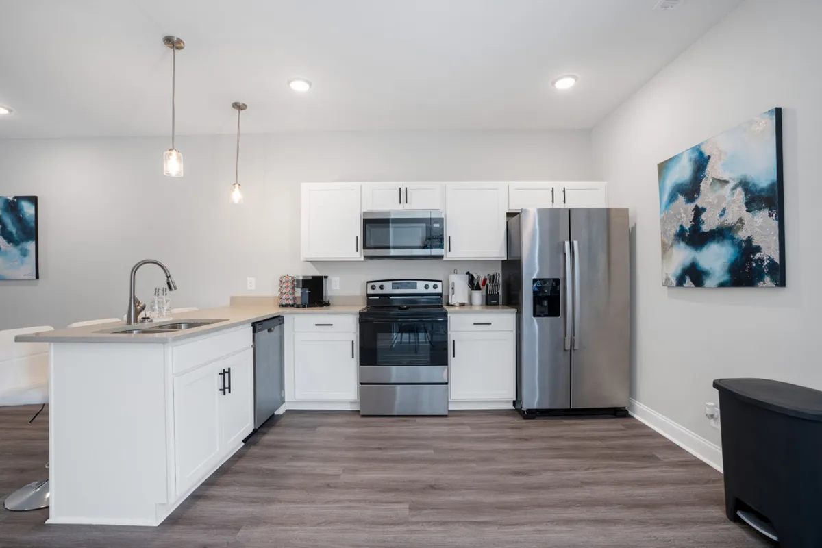 A bright, modern kitchen featuring an island in the center, sleek stainless steel appliances, and tasteful wall art. The space radiates functionality with ample counter space and open areas for meal prep or social interaction.