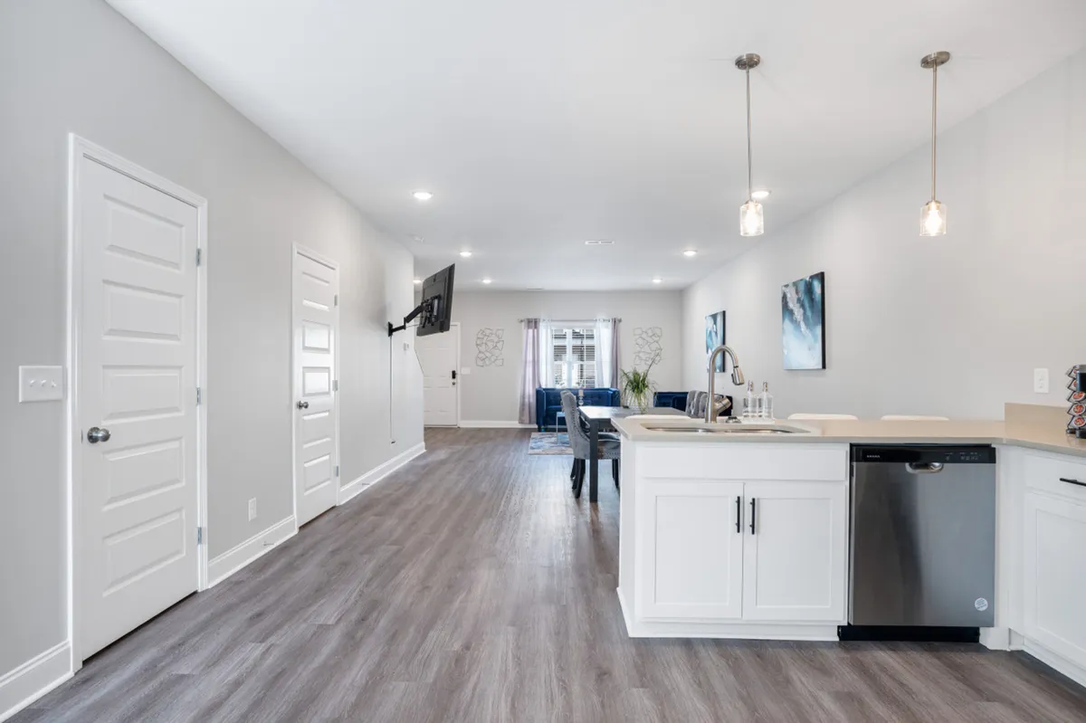 This image captures a seamless open-concept space where the kitchen island, dining area, and living room seating flow into one another. A TV mounted on the wall ties the areas together, while ample lighting and tasteful decor create an inviting, welcoming atmosphere.