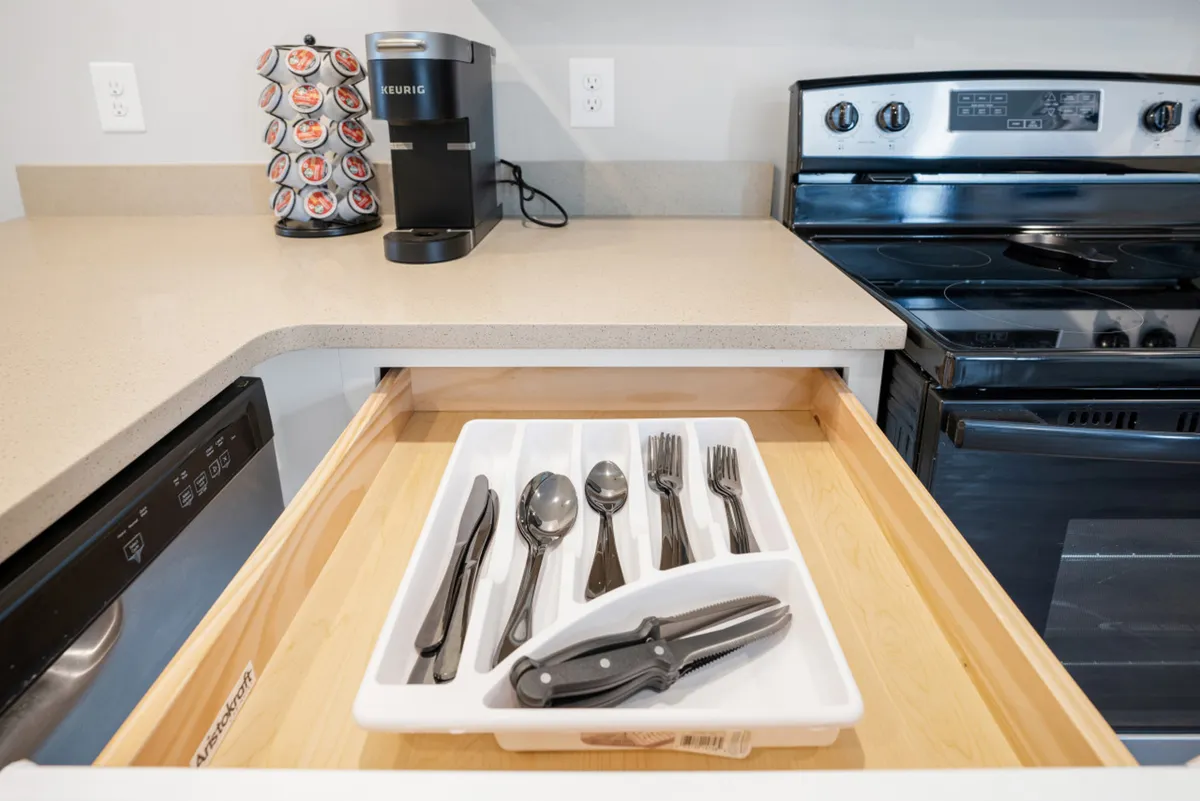 A functional and well-equipped kitchen with a cutlery drawer, coffee maker, and stove in view. The setting is warm and inviting, ideal for preparing group meals or enjoying a casual breakfast together.