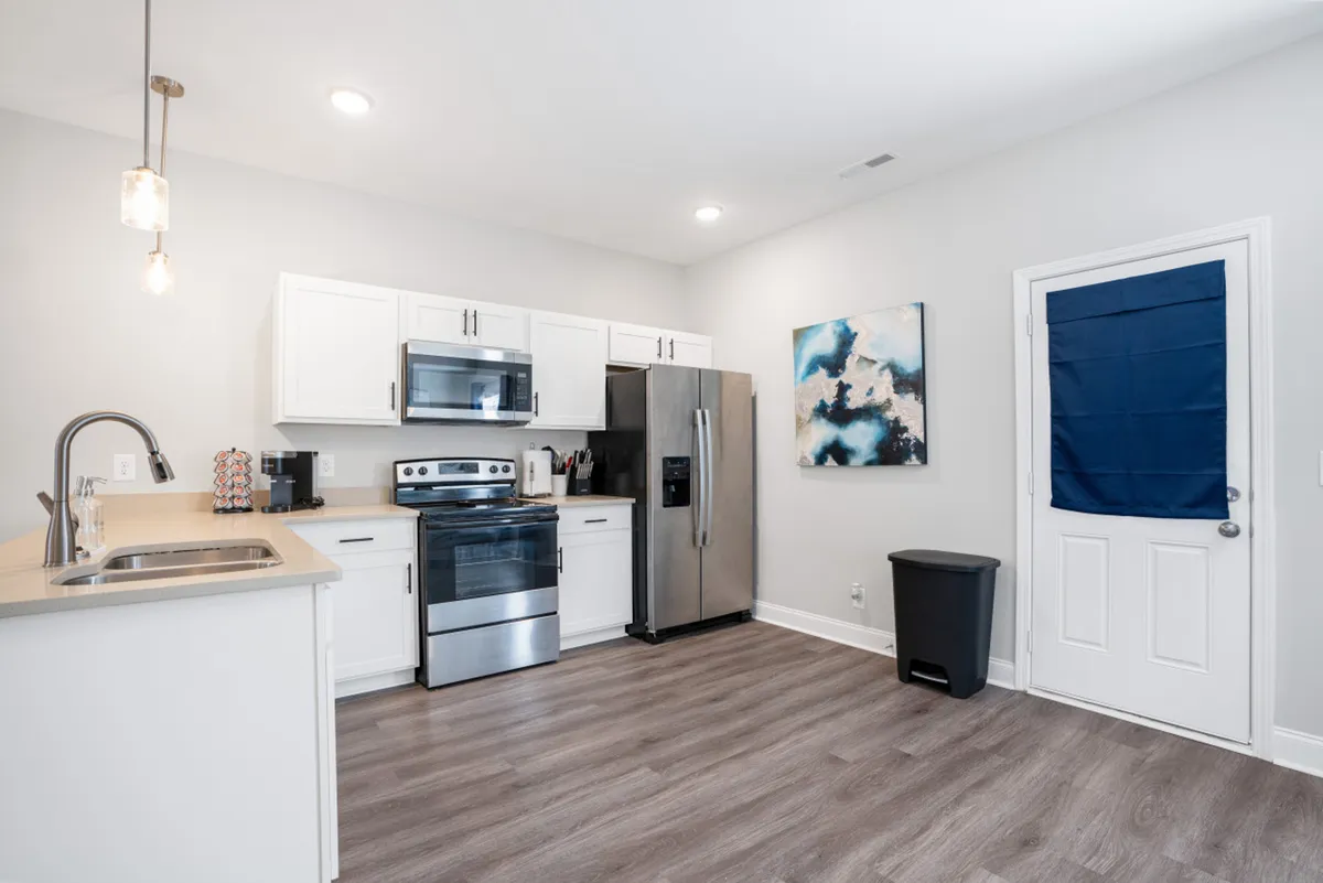A well-lit kitchen area showcasing stainless steel appliances, pristine white cabinetry, and a decorative piece of artwork on the wall. The design combines utility and warmth, emphasizing both style and a welcoming atmosphere for meal preparation and gatherings.