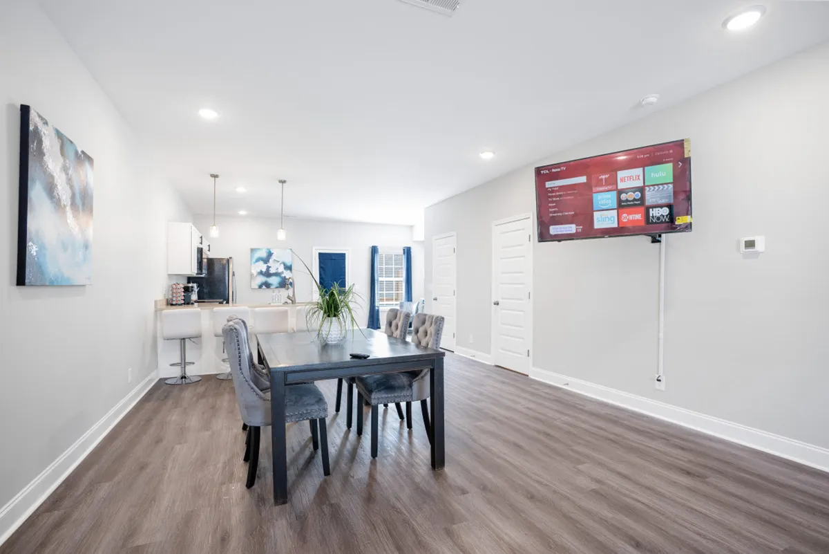 An open-concept interior combining the dining area and kitchen. The dining table is set near the kitchen, with a television and artwork visible on the wall, reflecting a space that adapts to both family dinners and casual gatherings with friends.
