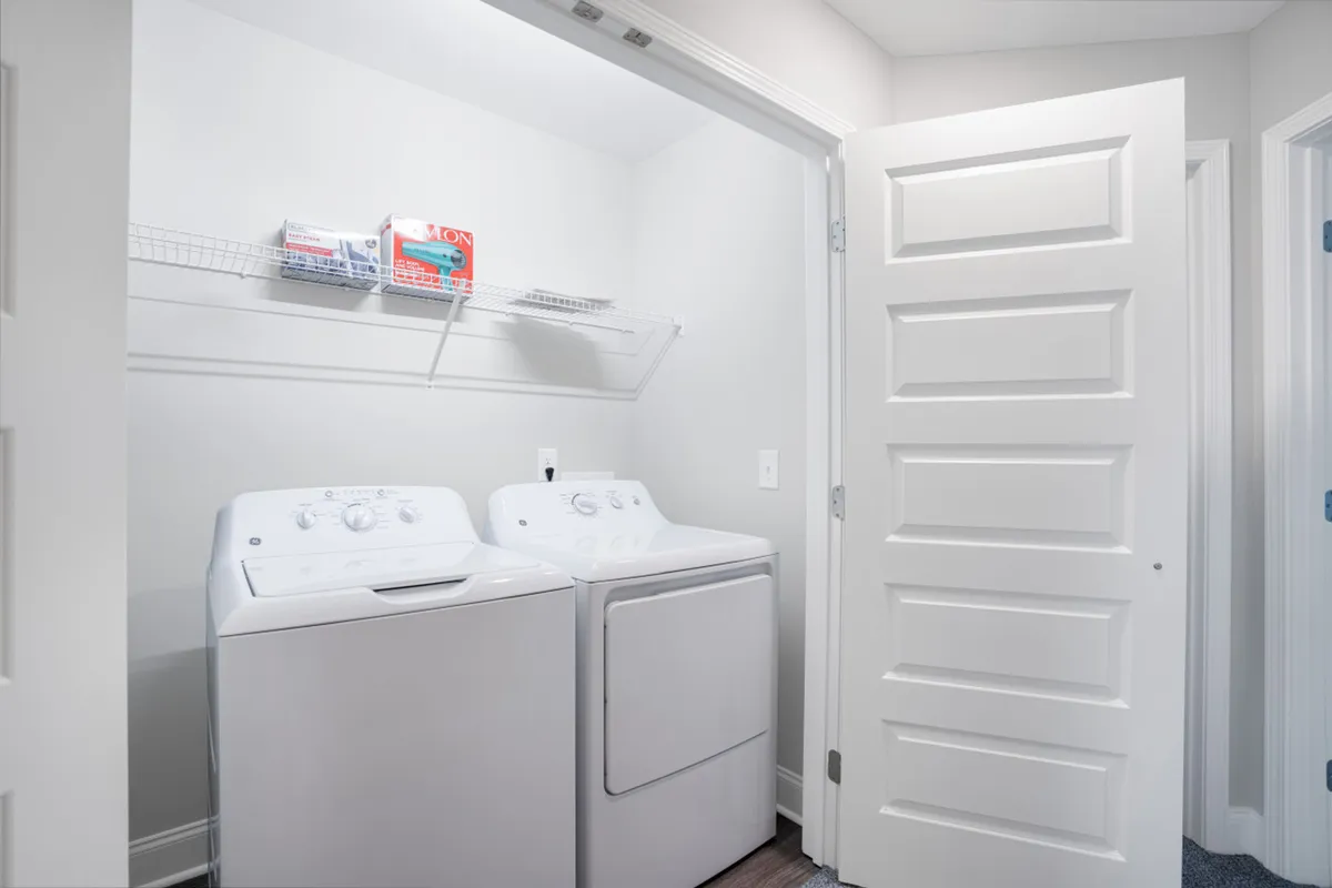 This image features a dedicated laundry area with a washing machine and dryer, along with a shelf stocked with various laundry supplies. The space is neat, organized, and clearly set up for convenient laundry use.